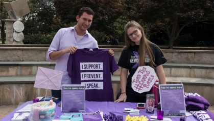 two students work stand behind a table with flyers, t-shirts, and giveaways to promote Turn the Campus Purple on Livginston camppus