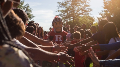 group of people stretch out their hands to high-five scarlet knight mascot