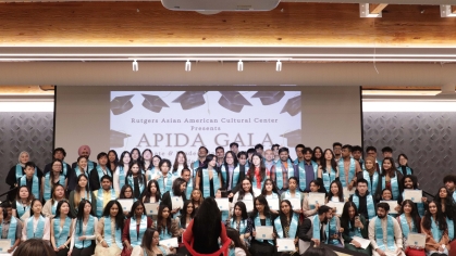Graduating APIDA students prepare to pose for a photo together; program coordinator Naima Chowdhury stands in the center of the photograph.